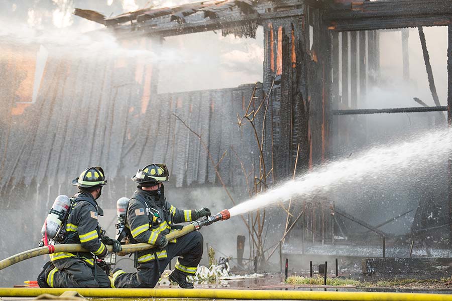 Two firefighters holding a hose and spraying a burning building